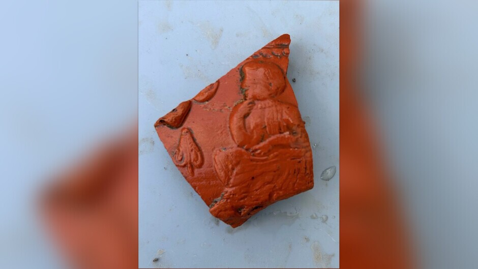 Scherbe einer Schüssel, die um 150 n. Chr. in Sinzig hergestellt wurde. [Beschreibung der Reliefverzierung: auf einem Stuhl sitzende Figur und ein Blatt]